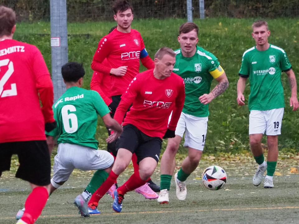 Spielszene mit Spielern in grünen und roten Trikots auf dem Kunstrasen