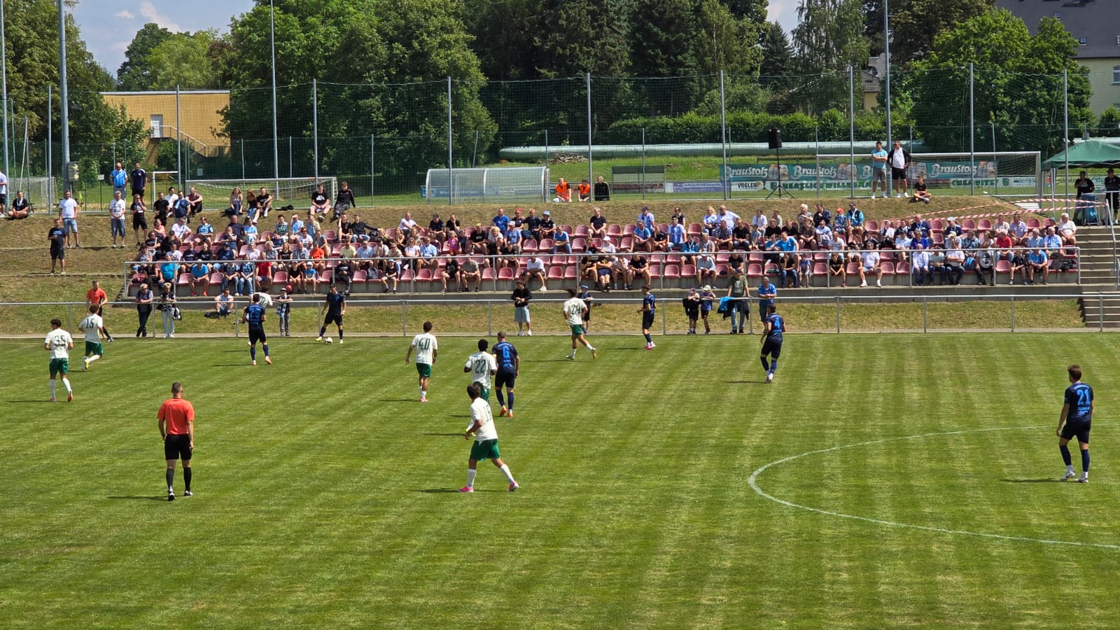 Spielszene im Stadion, im Hintergrund Zuschauer auf den Sitzschalen der Tribüne