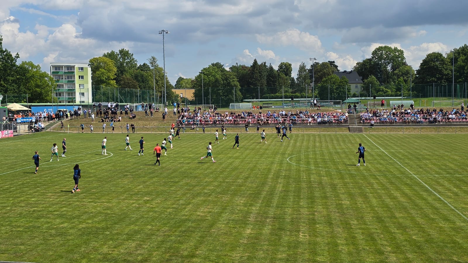 Weiter Blick über den Rasen auf die voll besetzte Tribüne des Stadions