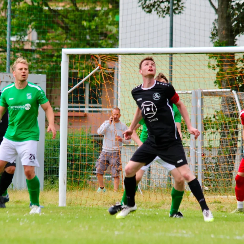 Zwei Spieler beobachten vor dem Tor den heranfliegenden Ball
